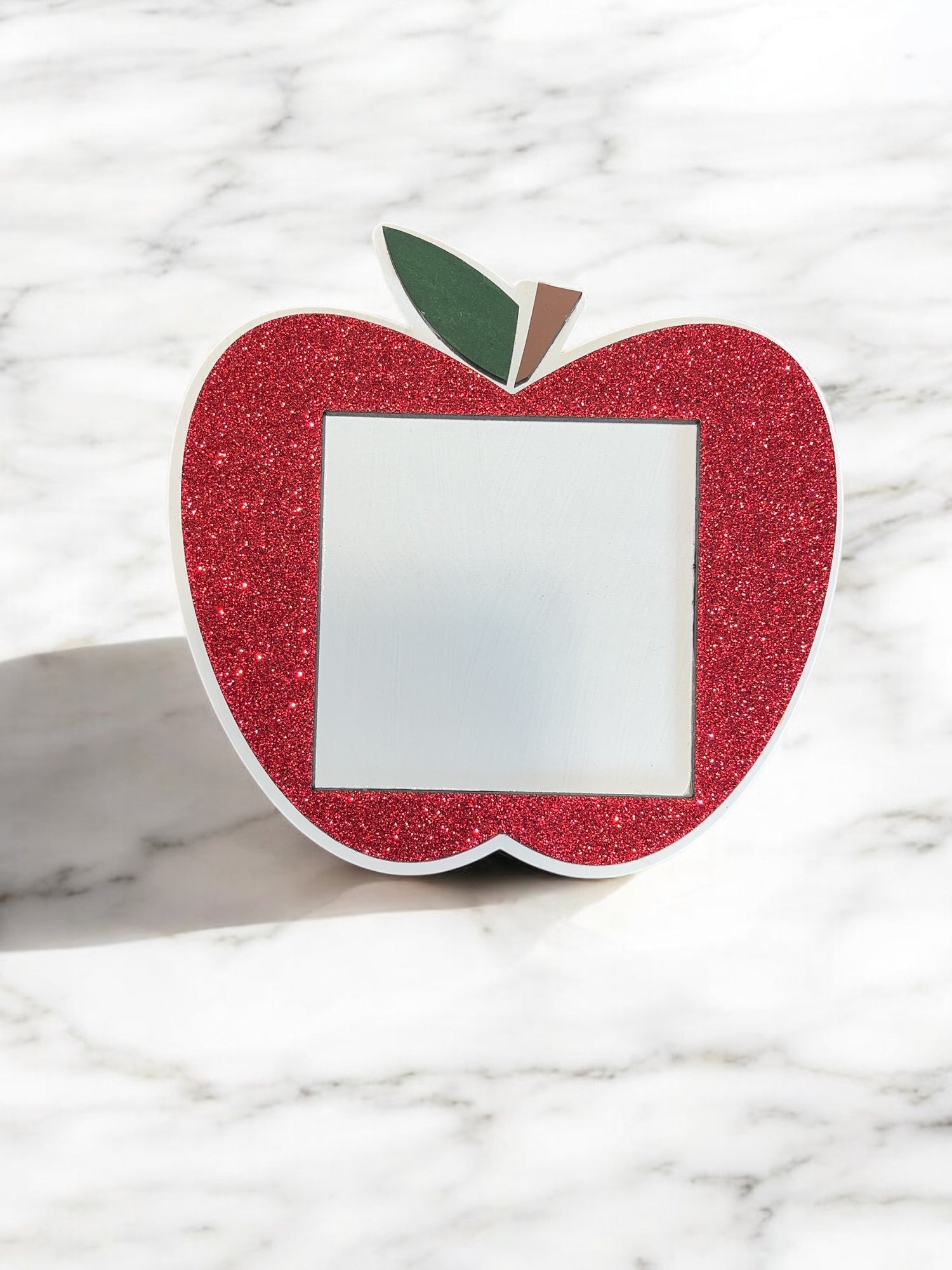 Apple-shaped Post-It Note holder with red glitter finish and green leaf detail, designed for standard sticky notes, on a marble background.