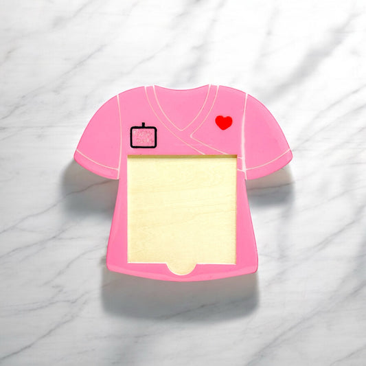 Pink nurse scrub top-shaped sticky note holder with a small heart and name badge details, designed to hold standard-sized Post-it Notes on a marble surface.