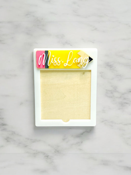 Custom teacher Post-It Note holder with a pencil-shaped nameplate personalized as "Miss. Lang," designed to fit standard-sized sticky notes, on a marble background.